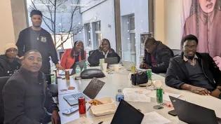 Seven Mastercard Foundation scholars sitting at a long table with laptops.