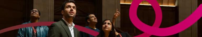 Five young professionals standing in a room looking up and pointing at the ceiling. 