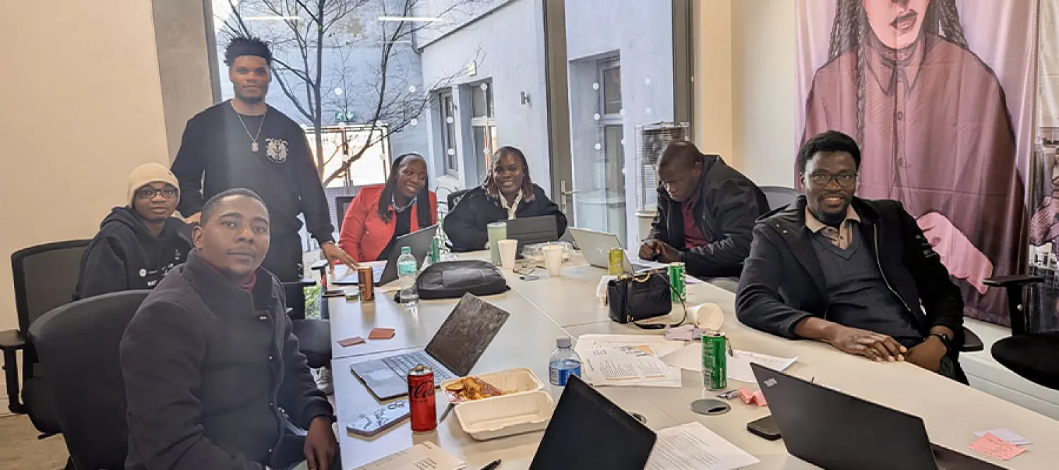 Seven Mastercard Foundation scholars sitting at a long table with laptops.