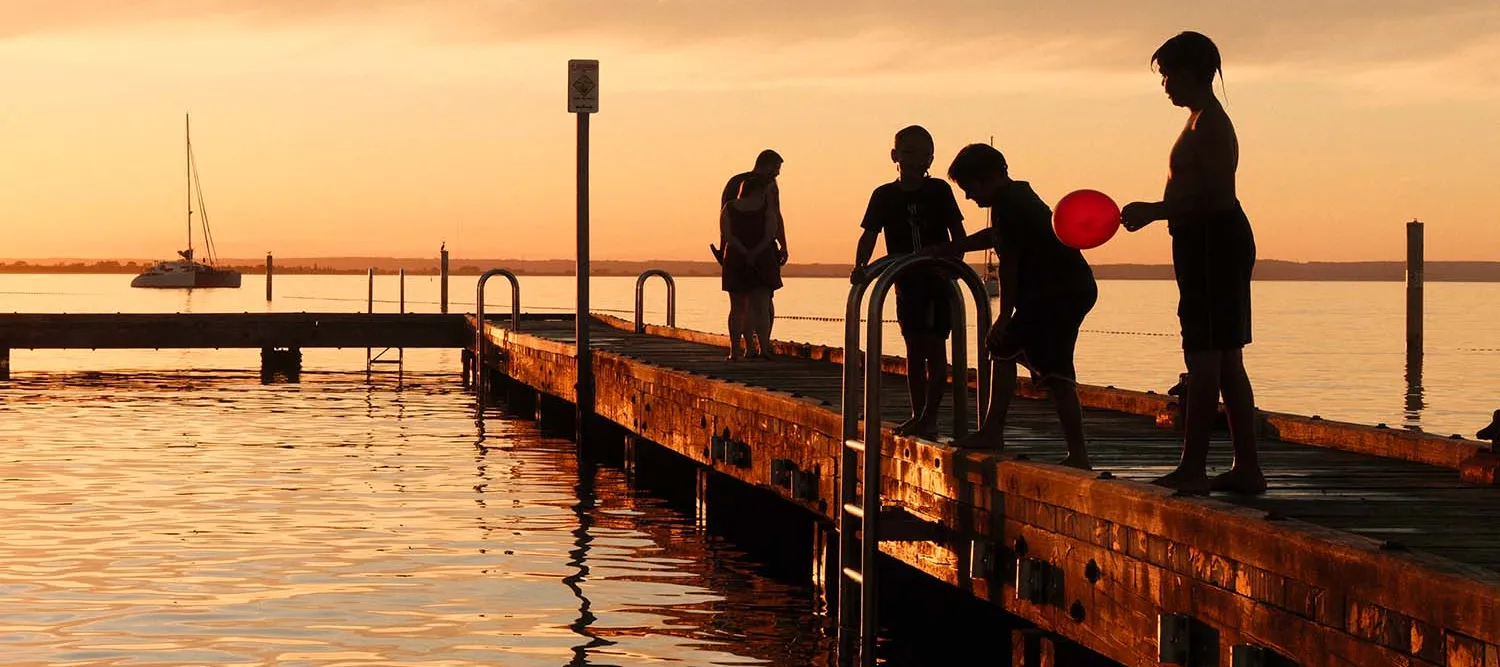 A group of children playing on a jetty at sunset.
