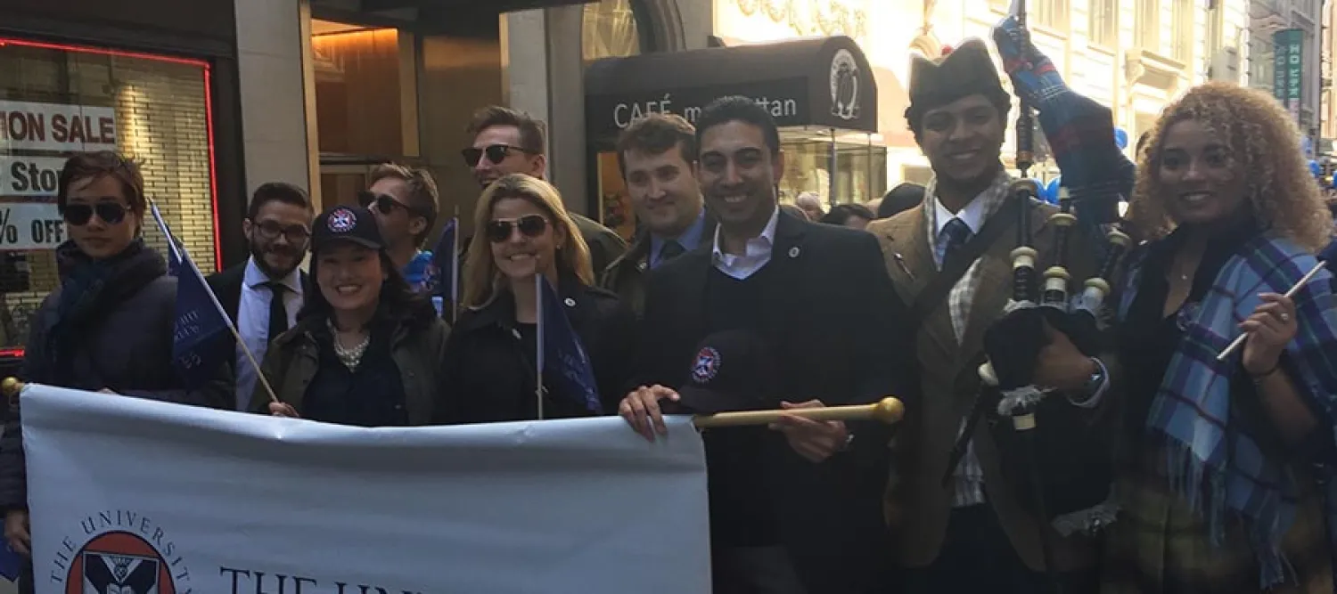 A group of people holding a sign and wearing tartan at a parade.