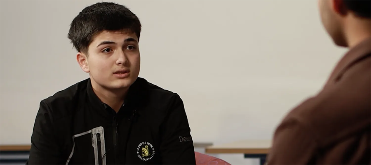 A young person sitting and speaking to a person out of focus.