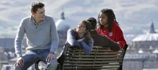 University of Edinburgh students sit on a bench with Edinburgh skyline behind them