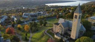 A drone shot of Cornell University, showing a building and tall spire surrounded by green grass and orange trees.