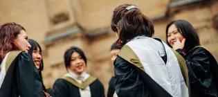 Six students in graduation robes standing in a circle and talking.