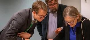 Three people looking down at something out of frame.