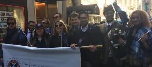 A group of people holding a sign and wearing tartan at a parade.