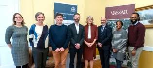 Eight people standing and smiling in front of signs that read "Vassar" and "the University of Edinburgh".