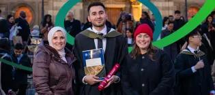 Two people standing and smiling with a person in graduation robes holding their graduation certificate