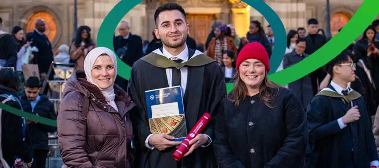 Two people standing and smiling with a person in graduation robes holding their graduation certificate