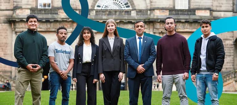 Seven students in professional attire standing and smiling outside the University's Old College.