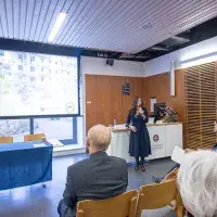 A person in a classroom standing in front of a projector screen speaking to a group.