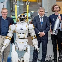 Seven people standing in a robotics lab, smiling with a humanoid robot.