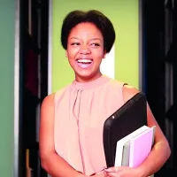 A student, Briana Pegado, smiling while holding books and a laptop.