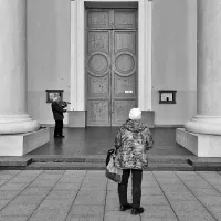 A person looking at a large door. The image is in black and white.