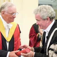 Neil Armstrong in ceremonial robes bring handed a degree in a red tube.