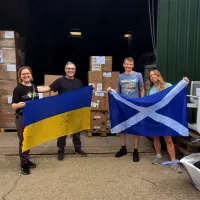 Man and woman holding Ukraine flag beside man and woman holding Scotland flag in front of warehouse