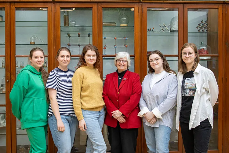 Six people standing and smiling in front of a cabinet filled with scientific devices.