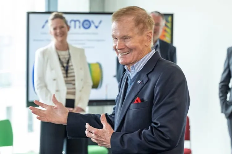 Bill Nelson smiling and talking to a group. Other people in professional attire can be seen in the background.