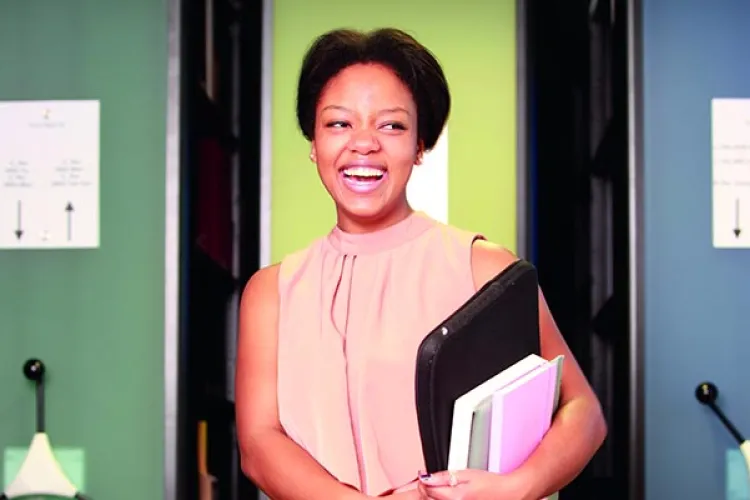 A student, Briana Pegado, smiling while holding books and a laptop.