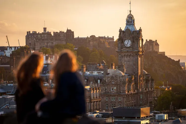 Two people looking out at a clocktower with Edinburgh Castle visible in the background.