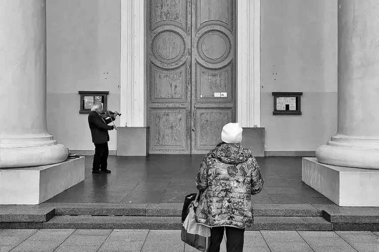 A person looking at a large door. The image is in black and white.