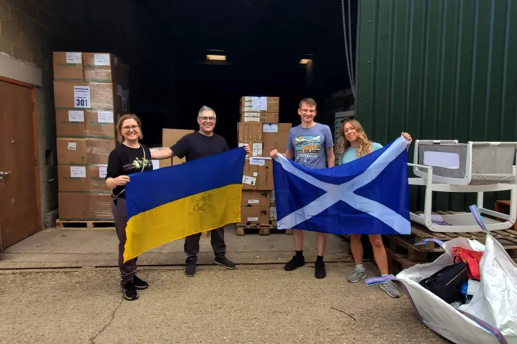 Man and woman holding Ukraine flag beside man and woman holding Scotland flag in front of warehouse