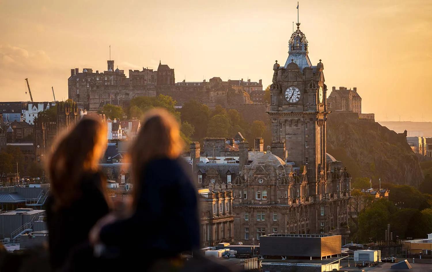Two people looking out at a clocktower with Edinburgh Castle visible in the background.