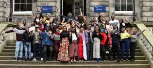 A large group of Mastercard Foundation Scholars posing happily outside a University building.