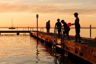 A group of children playing on a jetty at sunset.