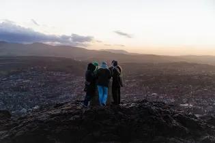 People huddled in a group overlooking Edinburgh city at sunset.