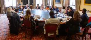 A large group of people in professional attire sitting and talking around a round table.
