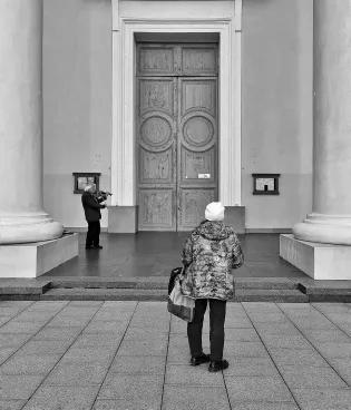 A person looking at a large door. The image is in black and white.