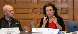 Two people, including Liz Grant, sitting in a board room speaking.