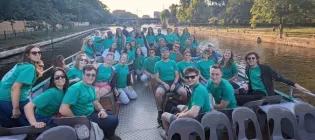 A large group of students sitting on a boat going over a river. The students are wearing matching green shirts and are smiling at the camera.